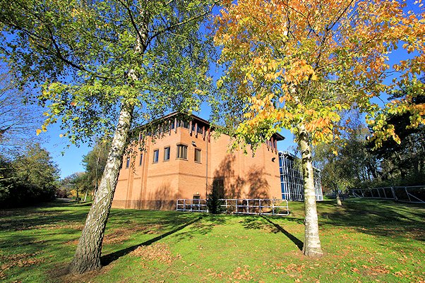 Rear of a large modern building, with trees - one with autumnal colours - in the sunshine