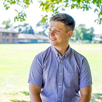 Portrait shot of young man with Back Field and buildings beyond, on a sunny summer's day